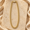 Cadena cubana de eslabones lisos en tono dorado con cierre rectangular decorado con piedras transparentes, sobre piedra crema y satén.