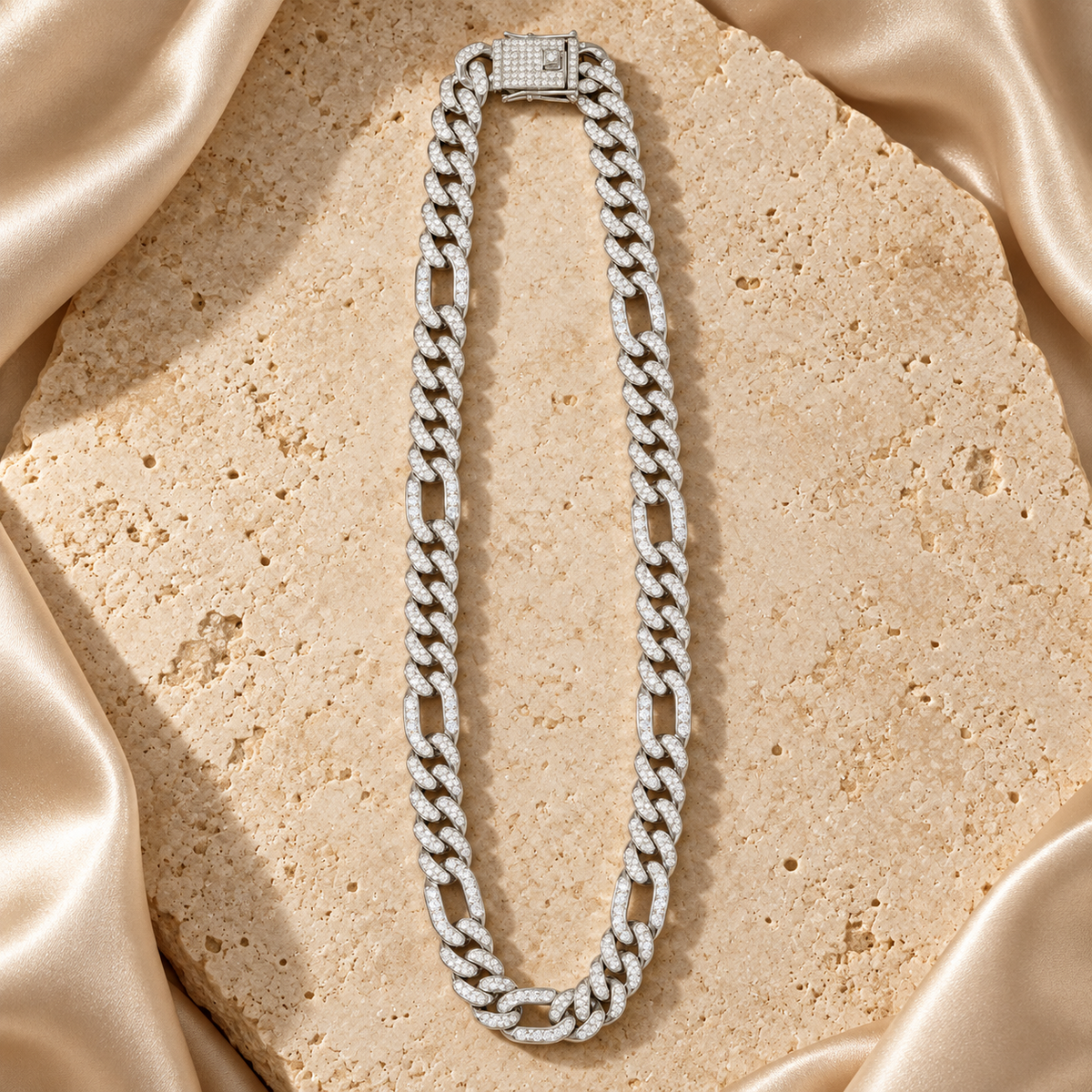 Cadena en tono plateado con grupos de eslabones cortos y eslabones alargados, cubierta de piedras transparentes y con cierre rectangular brillante.