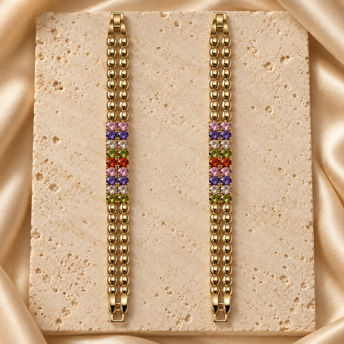 Par de dos pulseras en tono dorado con dos hileras de eslabones ovalados y piedras redondas multicolor en el centro.