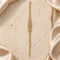 Pulsera en tono dorado con placa calada de 15 Años, dos flores de piedras transparentes, eslabones de espiral y cadena de extensión.