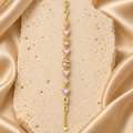 Una pulsera en tono dorado con cuatro corazones facetados iridiscentes, figuras de búho, elefante y flor, cierre de langosta y cadena de extensión.