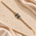 Pulsera dorada con dos piedras facetadas iridiscentes, detalles florales en tonos rosado y plateado, y extensión con dije de corazón.