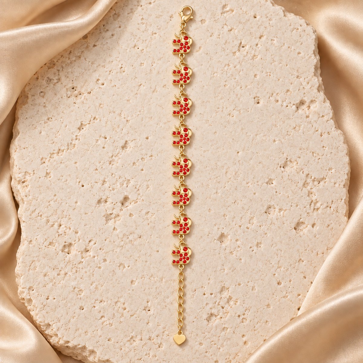 Una pulsera en tono dorado con ocho elefantes de trompa elevada, piedras rojas, cierre de langosta y cadena de extensión con terminal de corazón.
