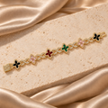 Pulsera en tono dorado con seis flores en color multicolor, eslabones de infinito con brillo y cierre rectangular de piedras transparentes.