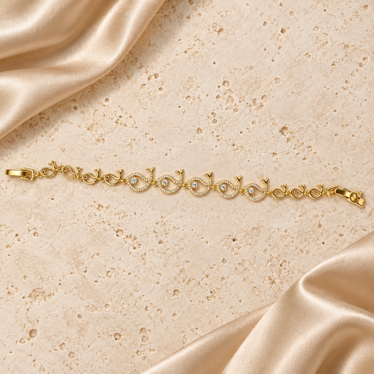 Una pulsera en tono dorado con cinco peces grandes de piedras transparentes, pequeños eslabones de pez y cierre plegable completo.