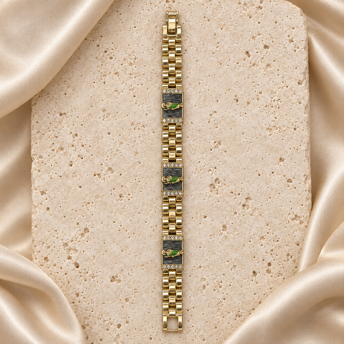 Una pulsera en tono dorado con tres placas de fondo negro, figuras de San Judas, filas de piedras transparentes y cierre plegable.