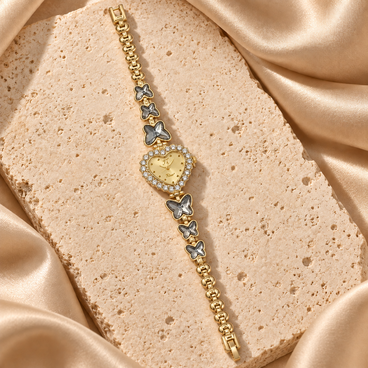 Reloj de pulsera dorado con carátula de corazón rodeada de piedras transparentes y seis mariposas gris humo.