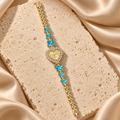 Reloj de pulsera dorado con carátula de corazón rodeada de piedras transparentes y seis mariposas turquesas.