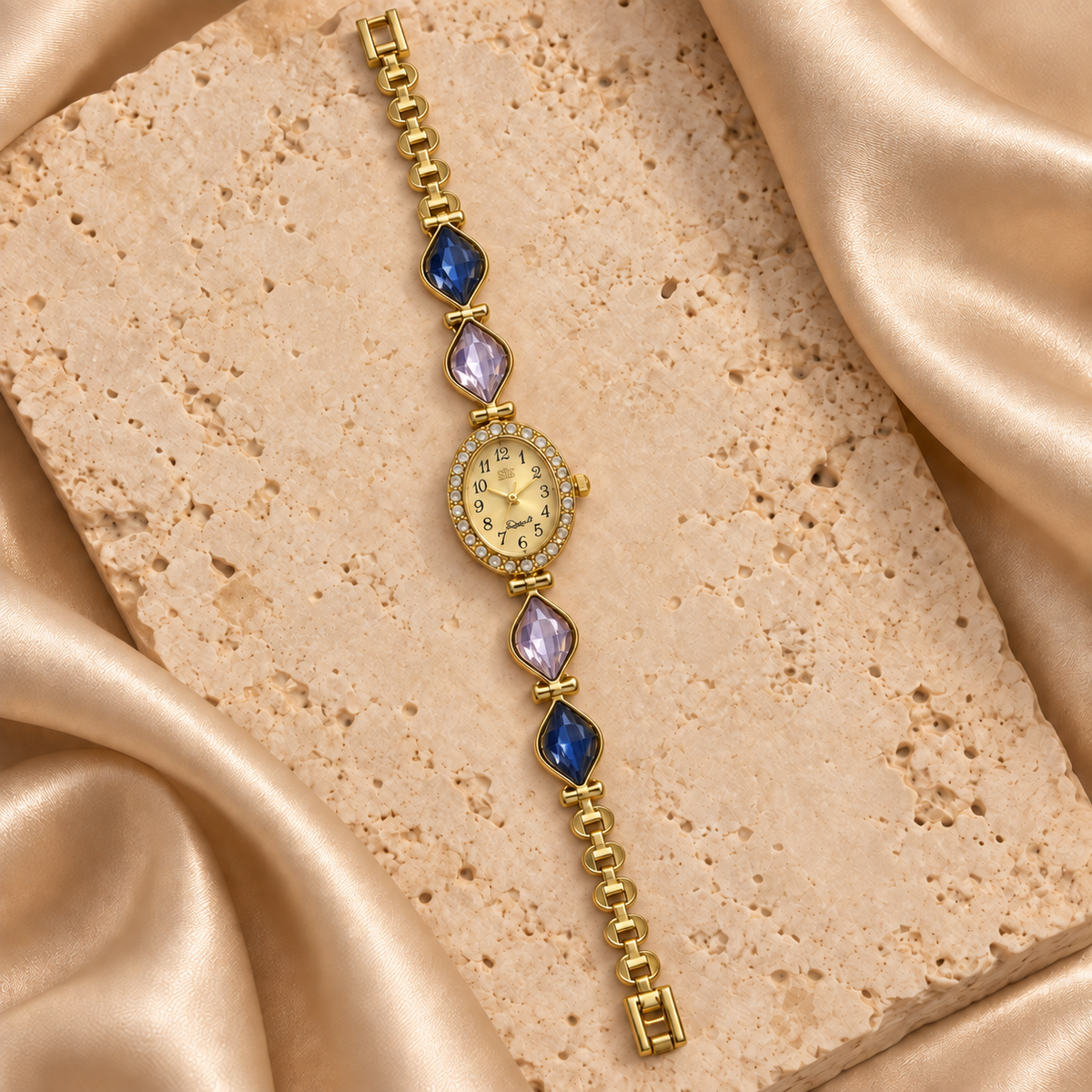 Reloj dorado con carátula ovalada, contorno de piedras transparentes y cuatro hojas facetadas azules y lilas.