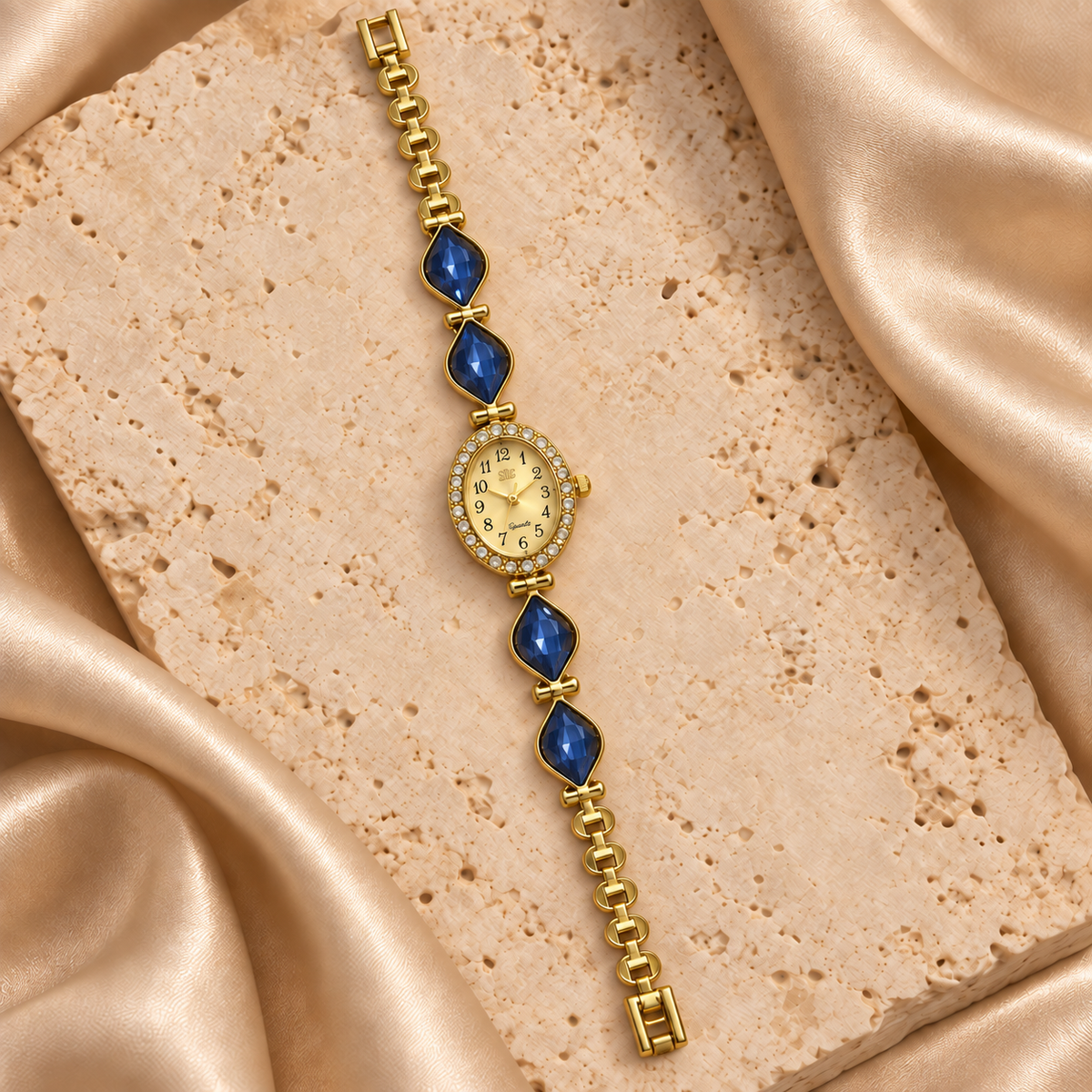 Reloj dorado con carátula ovalada, contorno de piedras transparentes y cuatro hojas facetadas azul oscuro.