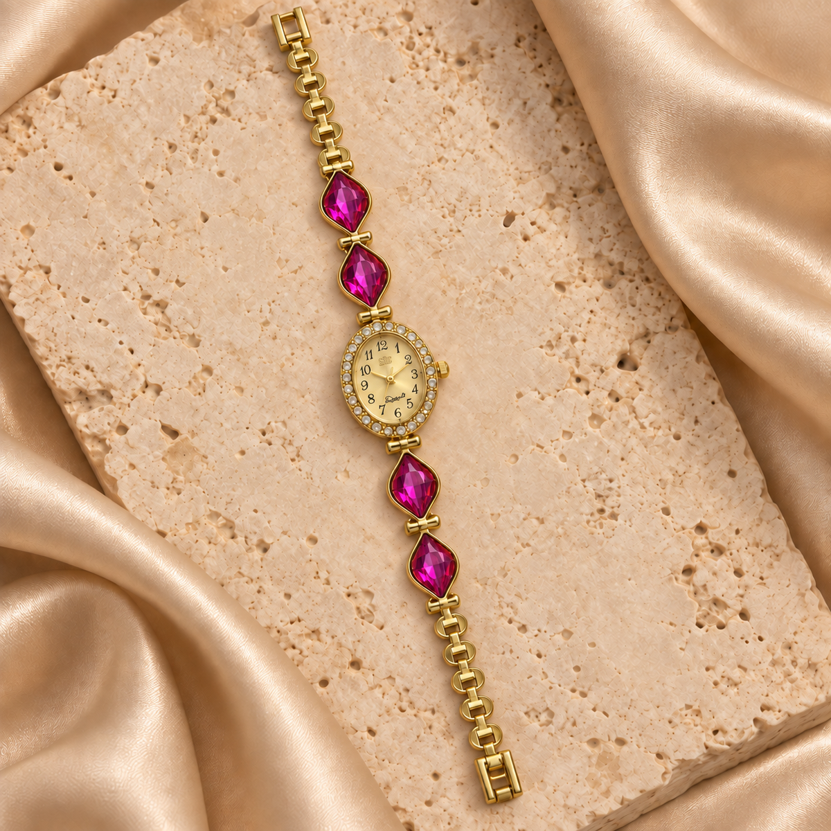 Reloj dorado con carátula ovalada, contorno de piedras transparentes y cuatro hojas facetadas fucsias.