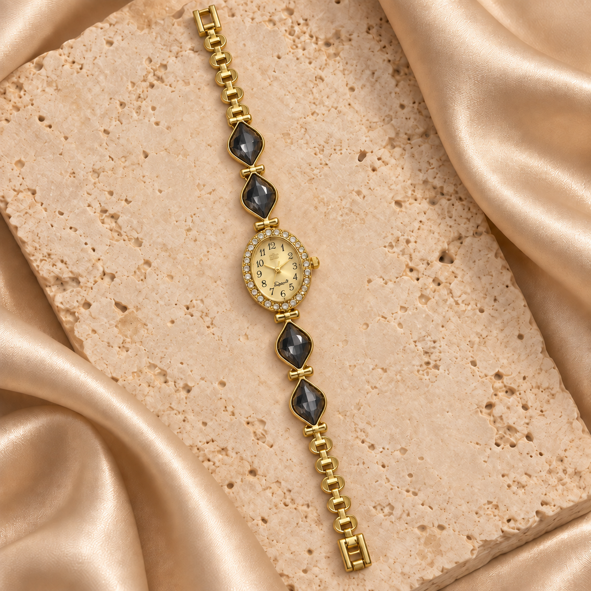 Reloj dorado con carátula ovalada, contorno de piedras transparentes y cuatro hojas facetadas negras.