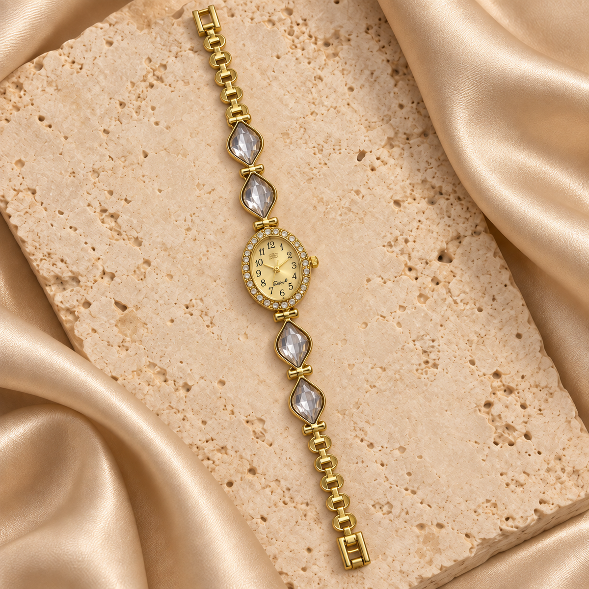 Reloj dorado con carátula ovalada, contorno de piedras transparentes y cuatro hojas facetadas transparentes.