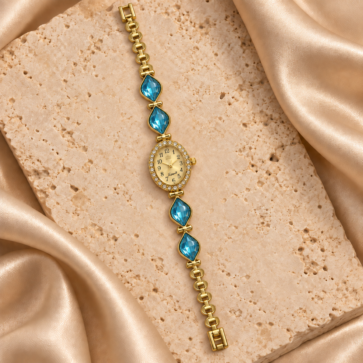 Reloj dorado con carátula ovalada, contorno de piedras transparentes y cuatro hojas facetadas turquesas.