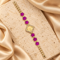 Reloj dorado con carátula de trébol rodeada de piedras transparentes y seis flores fucsias facetadas sobre una pulsera de eslabones.