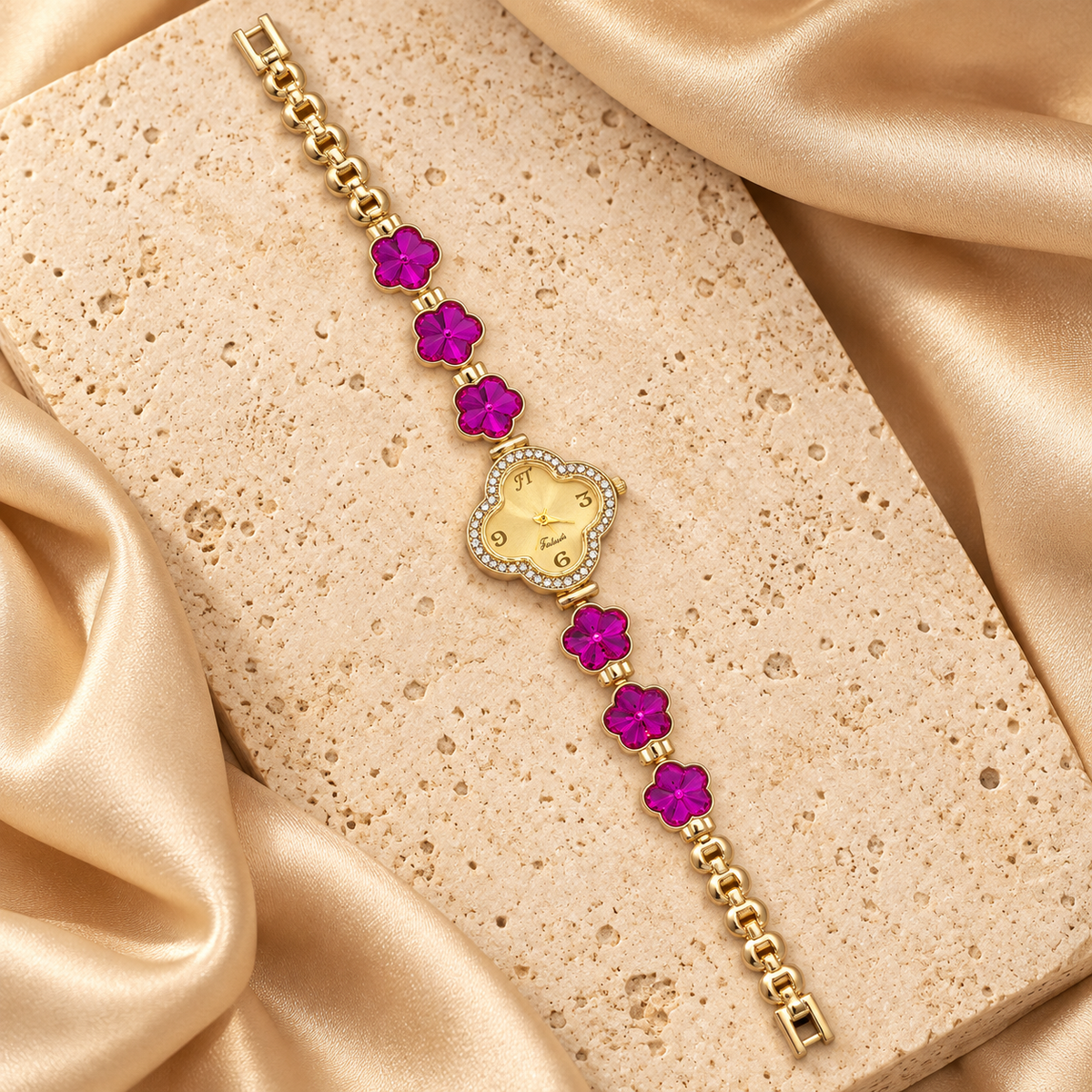 Reloj dorado con carátula de trébol rodeada de piedras transparentes y seis flores fucsias facetadas sobre una pulsera de eslabones.