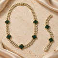 Cadena de eslabones dorados con cinco tréboles verdes y piedras transparentes, junto a una pulsera a juego con dos tréboles y cierre rectangular.