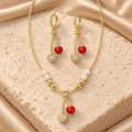 Collar dorado con ocho cuentas blancas y doradas y dije de cerezas rojas y brillantes, acompañado de dos aretes largos de cerezas a juego.