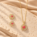 Collar dorado con dije de flor abierta, centro rojo coral y detalles brillantes transparentes, acompañado de dos aretes florales a juego.