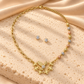 Collar dorado asimétrico con nueve cuentas tricolor y dije de aves con alas extendidas, acompañado de dos aretes redondos brillantes.