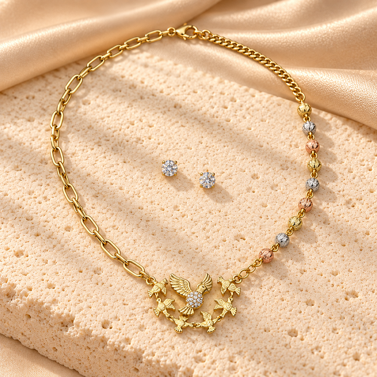 Collar dorado asimétrico con nueve cuentas tricolor y dije de aves con alas extendidas, acompañado de dos aretes redondos brillantes.