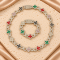 Set de collar y pulsera con flores de cuatro pétalos rojos, verdes, rosas, oscuros y transparentes, unidas por eslabones de infinito brillantes.