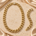 Cadena y pulsera en tono dorado con eslabones anchos, lisos y entrelazados, y cierres rectangulares decorados con piedras transparentes.